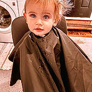 Hayes joined the competition — help win amazing prizes! toddler, child, haircut, cape, chair, washing_machine, laundry_room, face, eyes, hair, expression, indoors, door, mat, clothing, person, portrait, seated, curious, cute