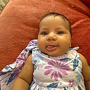 Saphire joined the competition — help win amazing prizes! baby, infant, child, couch, red_couch, floral_dress, tongue_out, toy, colorful_toy, indoor, smiling, happy, cute, face, skin, person, sitting, fabric, home, playful