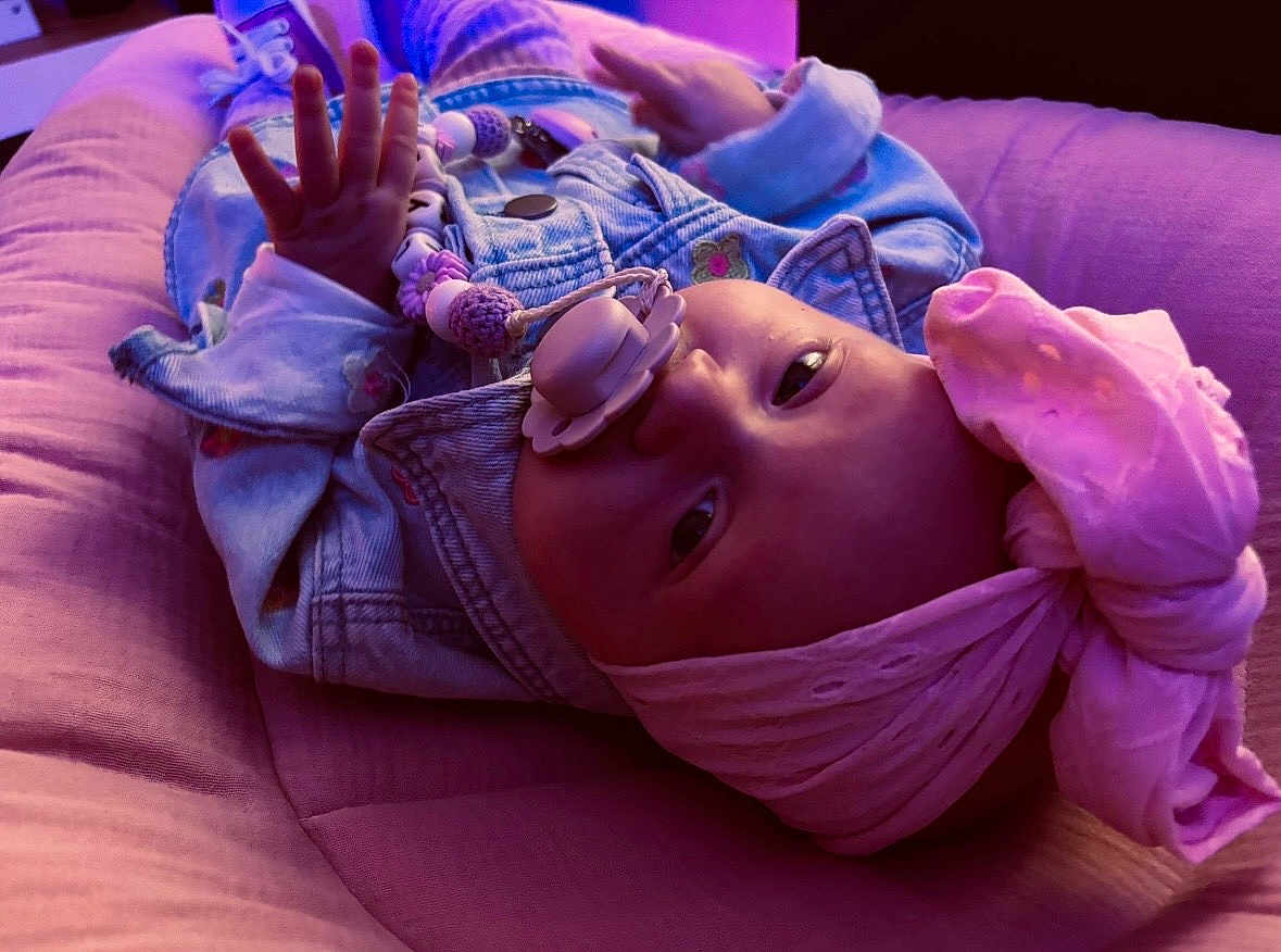 Lyla participe au concours pour gagner de l'argent avec cette photo : baby, infant, pacifier, pacifier_clip, headwrap, bandana, pink, purple, denim_jacket, closeup, portrait, lying_down, hand, bedding, blanket, nursery, cute, accessory, beads, indoors