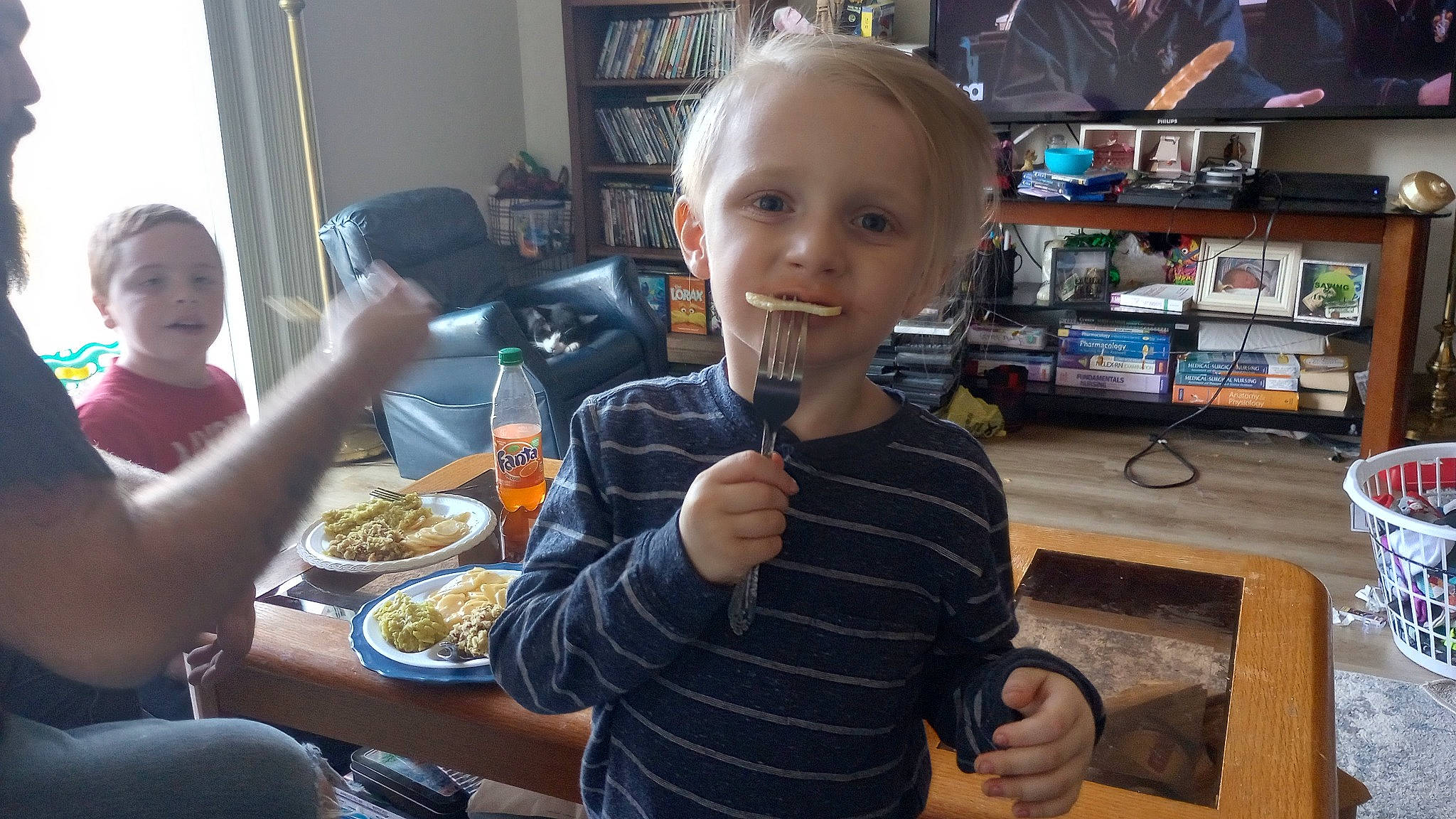 Jax is registered to the contest to win money with this photo: arm, bookcase, bowl, chair, child, comfort_food, food, food_craving, fun, junk_food, person, plate, room, sharing, shelf, shelving, sitting, t_shirt, table, tableware