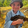 child, kid, toddler, hat, bucket_hat, chicken, hen, poultry, farm, straw, outdoors, blue_shirt, smile, portrait, holding, sunny, nature, cheeks, rural, animal