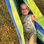 Alinoë participe au concours pour gagner de l'argent avec cette photo : child, toddler, baby, face, smile, hammock, striped_hammock, onesie, sleepwear, outdoor, grass, summer, relaxing, lying_down, portrait, blue, green, eyes, happy, playtime