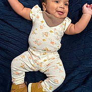 Aurora is registered to the contest to win money with this photo: baby, infant, smiling, face, arms, floral_outfit, sneakers, brown_shoes, blanket, textured_blanket, lying_down, happy, cute, child, person, indoors, apparel, footwear, skin, head