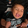 Aurora is registered to the contest to win money with this photo: baby, child, laughing, smiling, person, face, curly_hair, black_clothing, philadelphia_eagles, sportswear, eagles_logo, hands, adult, joy, happiness, closeup, indoor, portrait, team_spirit, celebration