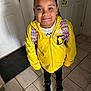 child, yellow_hoodie, backpack, indoor, tile_floor, smiling, standing, black_shoes, braided_hair, door, doormat, casual_clothing, young, person, portrait, ready_for_school, happy, home, fashion, looking_up