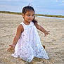 child, beach, sand, dress, white_dress, silver_hearts, girl, playful, arms_out, cloudy_sky, outdoor, nature, young_child, smile, sitting, portrait, happy, cute, daytime, fun