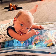 Tripp is registered to the contest to win money with this photo: baby, blurred_background, child, colorful, cute, expression, face, floor, footwear, hand, indoor, infant, inflatable_mat, lying_down, person, sandals, soft_light, striped_clothing, toddler, wooden_floor