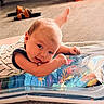 baby, blurred_background, child, colorful, cute, expression, face, floor, footwear, hand, indoor, infant, inflatable_mat, lying_down, person, sandals, soft_light, striped_clothing, toddler, wooden_floor