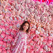 Luna is registered to the contest to win money with this photo: child, girl, smiling, curly_hair, dress, plush_toys, stuffed_animals, pink, white, hello_kitty, bunny, bear, neon_sign, wall, indoor, cute, happy, colorful, toy_display, floor