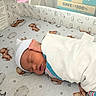 Enzo is registered to the contest to win money with this photo: newborn, baby, sleeping, crib, blanket, hat, teddy_bear, cloud, star, hospital, infant, bed, sleep, peaceful, swaddle, person, cute, soft_lighting, pattern, nursery