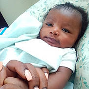 Kadeem is registered to the contest to win money with this photo: baby, infant, hand, holding_hands, blanket, manicure, nails, person, face, skin, white_clothing, bed, comfort, closeup, indoor, cute, calm, love, tenderness, family