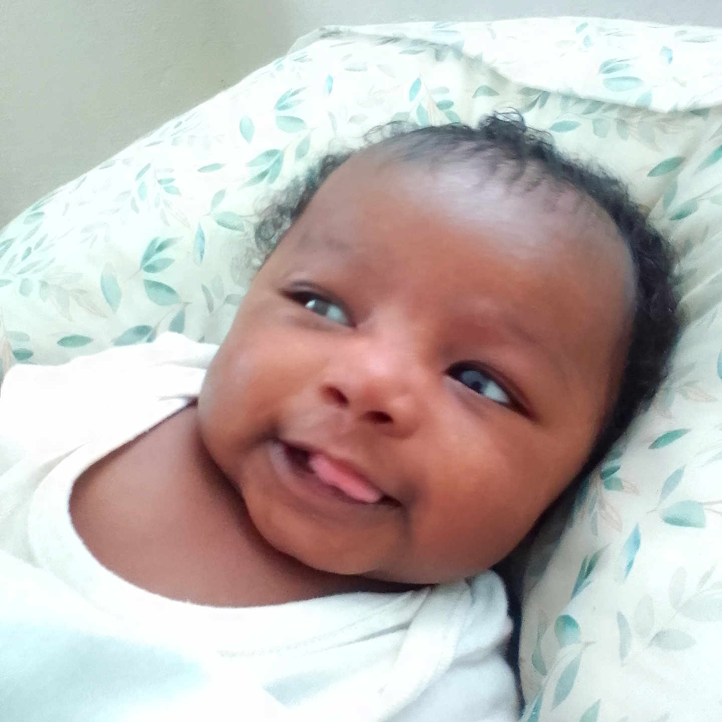 Kadeem is registered to the contest to win money with this photo: baby, cheeks, curly_hair, cute, expression, face, head, indoors, infant, lying_down, pattern, person, pillow, playful, skin, smile, soft_texture, tongue, white_clothing, young_child