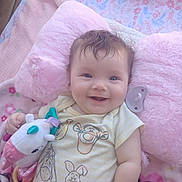 Maggie Sue joined the competition — help win amazing prizes! baby, smiling, toy, unicorn, pink_pillow, onesie, cute, child, infant, happy, face, hand, blanket, soft, lying_down, indoors, plush, comfort, toddler, portrait