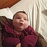 Maggie Sue is registered to the contest to win money with this photo: baby, infant, child, maroon_clothing, bed, hand, wooden_headboard, curious_expression, indoor, person, portrait, cute, chubby_cheeks, holding, adult_hand, sleeping_area, blanket, fabric, cozy, casual