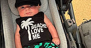 Maximus is registered to the contest to win money with this photo: baby, infant, stroller, cap, black_clothing, tropical_print, palm_tree, shorts, sleeveless_shirt, cute, child, outdoor, sunny, seat, fabric, person, legs, expression, casual, summer