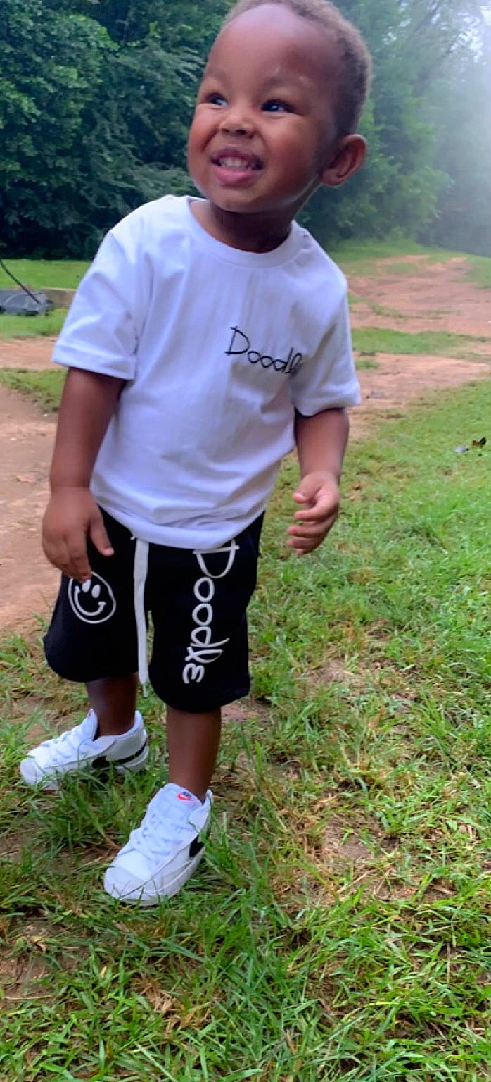 Harrison is registered to the contest to win money with this photo: active_shorts, baseball_cap, board_short, cap, child, eyewear, fun, grass, grassland, joy, knee, person, personal_protective_equipment, plant, shorts, sleeve, sportswear, sweatpant, t_shirt, thigh