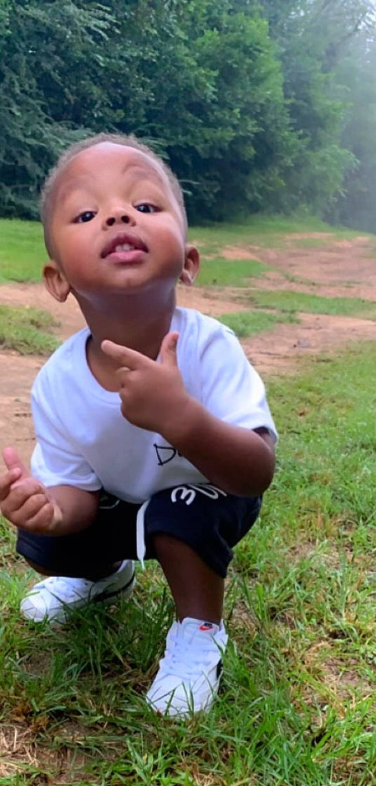 Harrison is registered to the contest to win money with this photo: baby_toddler_clothing, clothing, finger, gesture, grass, grass_family, grassland, hand, happy, leisure, meadow, people_in_nature, person, plant, shorts, sneakers, sock, t_shirt, thumb, toddler