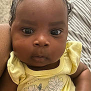 Imani joined the competition — help win amazing prizes! baby, child, clenched_fist, closeup, curly_hair, cute, expression, face, floral_print, hand, human, indoor, infant, natural_light, person, portrait, skin, soft_texture, yellow_clothing, young