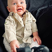Elliott is registered to the contest to win money with this photo: baby, child, infant, blue_eyes, shirt, pants, sitting, hand, face, smile, expression, indoor, clothing, footwear, portrait, young_child, cute, looking_up, person, background