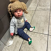 Jensen is registered to the contest to win money with this photo: baby, cardigan, child, corner, curious, cute, expression, face, floor, floor_tile, headwear, indoors, infant, knit_hat, person, plush, sitting, socks, tile, warm_clothing