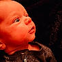 baby, infant, face, profile, onesie, clothing, stars, curious, looking_up, close_up, skin, head, child, young, human, warm_lighting, indoor, soft_texture, blanket, sleepwear