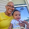 Azure is registered to the contest to win money with this photo: baby, casual, child, curtains, cute, daylight, family, glasses, happy, hello_kitty, holding, outdoor, person, plant, porch, portrait, smiling, window, woman, yellow_shirt
