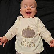 Ayla is registered to the contest to win money with this photo: baby, smiling, infant, pumpkin, sweatshirt, pants, pattern, lying_down, black_background, happy, child, cute, cozy, clothing, portrait, baby_clothes, infant_smile, small_child, indoor, casual