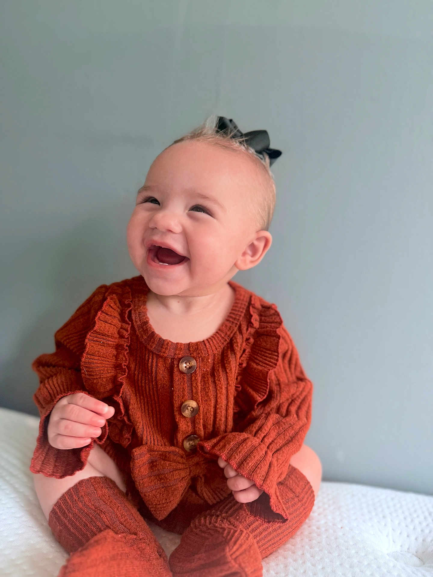 Amayah is registered to the contest to win money with this photo: baby, child, smiling, happy, sitting, knitwear, bow, cute, portrait, indoors, cozy, rust_color, socks, person, infant, closeup, headwear, buttoned, fashion, warm