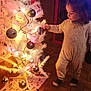 celebration, child, christmas, christmas_tree, cozy, curiosity, decorations, festive, floor, holiday, home, indoor, lights, ornaments, pajamas, person, toddler, toy, warm_lighting, wooden_paneling