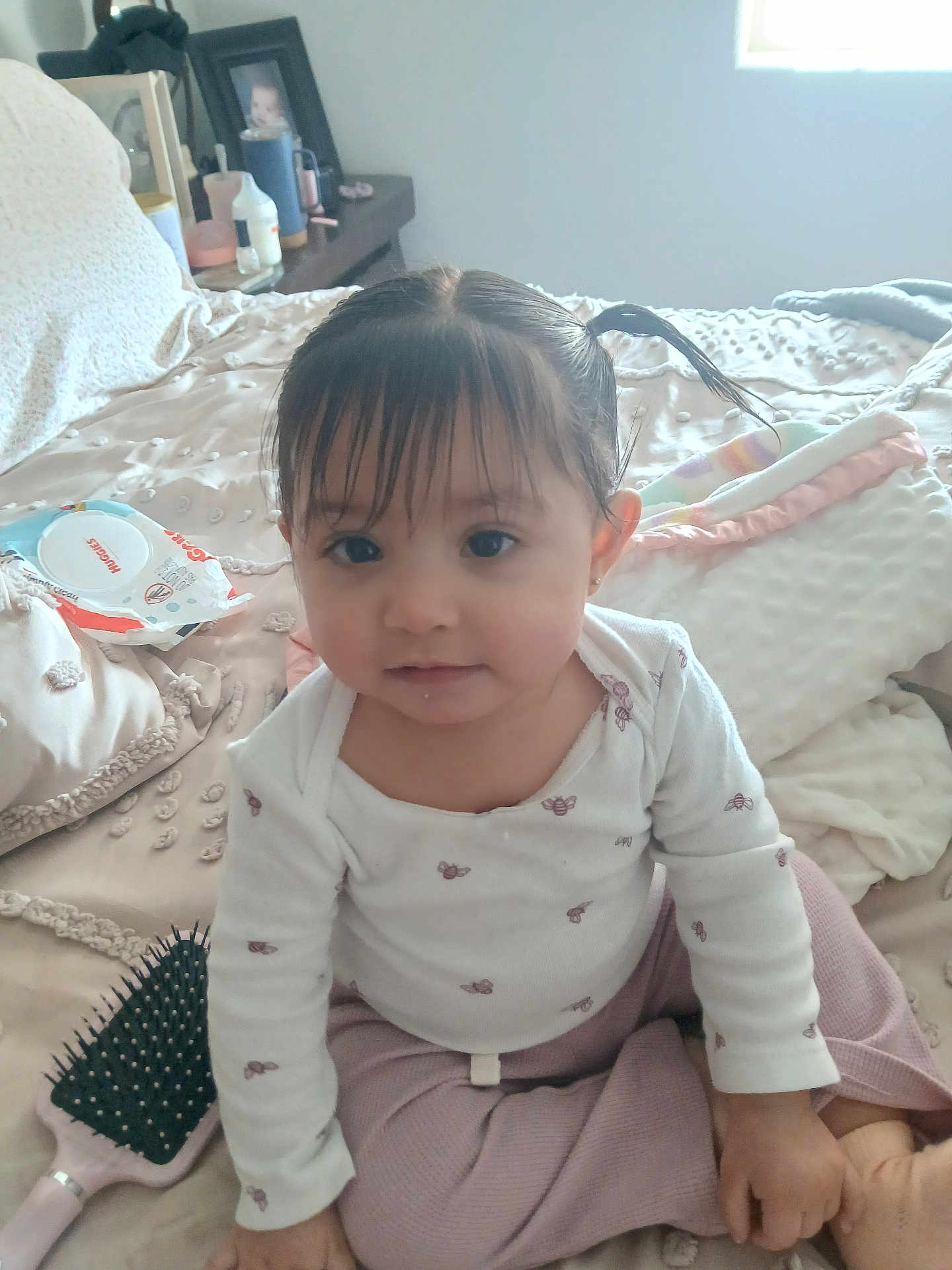 Aminah joined the competition — help win amazing prizes! baby, toddler, child, girl, pigtails, bangs, onesie, long_sleeve, sitting, bed, blanket, hairbrush, wipes, nightstand, window, portrait, indoors, cute, soft_lighting, smile
