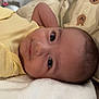 baby, infant, face, eyes, yellow_clothing, blanket, soft_texture, indoor, bag, animal_pattern, head, skin, person, lying_down, cute, closeup, child, newborn, cozy, expression