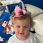 Leena is registered to the contest to win money with this photo: toddler, child, hat, pink, feather, white_shirt, blue_eyes, curly_hair, quilt, snowman, couch, indoor, portrait, smile, cute, rosy_cheeks, cozy, holiday, decor, furniture