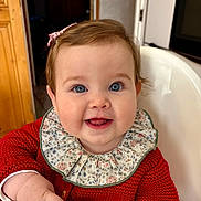 Victoire participe au concours pour gagner de l'argent avec cette photo : baby, child, smiling, blue_eyes, red_sweater, floral_collar, high_chair, indoors, cute, happy, face, hand, pacifier, person, infant, portrait, seated, clothing, furniture, warm_lighting