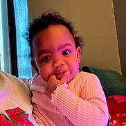 Symone is registered to the contest to win money with this photo: toddler, child, person, indoor, sweater, curly_hair, face, hand, cozy, couch, sitting, window, curtain, light, portrait, cute, expression, people, young, baby