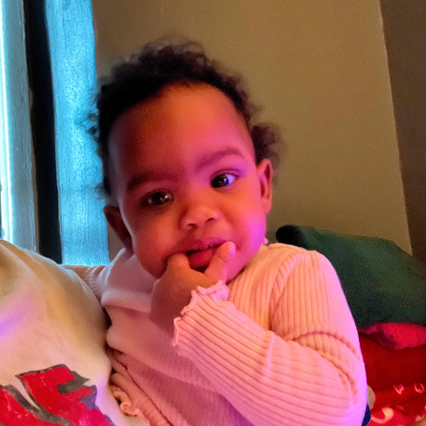 Symone is registered to the contest to win money with this photo: toddler, child, person, indoor, sweater, curly_hair, face, hand, cozy, couch, sitting, window, curtain, light, portrait, cute, expression, people, young, baby