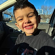 Maxwell is registered to the contest to win money with this photo: child, boy, smiling, teeth, car_interior, vehicle_window, sunlight, shadow, t_shirt, short_hair, happy, portrait, close_up, ear, cheek, dashboard, passenger_seat, basketball_hoop, outdoor_background, seat