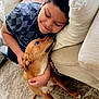 boy, dog, couch, carpet, smiling, affection, indoor, pet, child, love, casual_clothing, brown_dog, short_hair, hugging, closeup, cozy, home, interaction, warmth, domestic