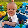 baby, child, infant, smiling, happy, portrait, face, outdoor, playground, activity_center, toys, colorful, seated, short_hair, white_shirt, blue_seat, green_grass, backyard, close_up, photography