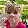 child, girl, blonde_hair, hair_clip, pink_shirt, close_up, face, outdoor, grass, sidewalk, chalk_drawing, bicycle, boy, pickup_truck, car, suburban, residential_area, daylight, casual_clothing, portrait