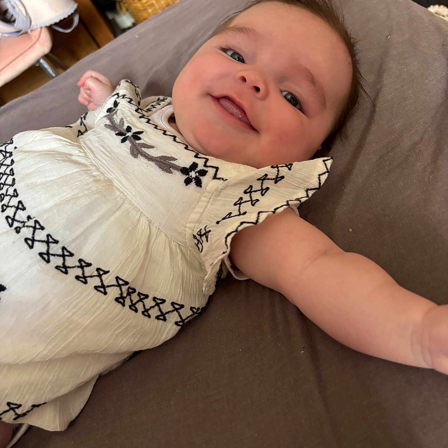 Elsie Rose is registered to the contest to win money with this photo: arm, baby, black_embroidery, child, closeup, cute, eyes, fabric, face, happy, head, indoor, infant, lying_down, mouth, person, portrait, skin, smiling, white_dress