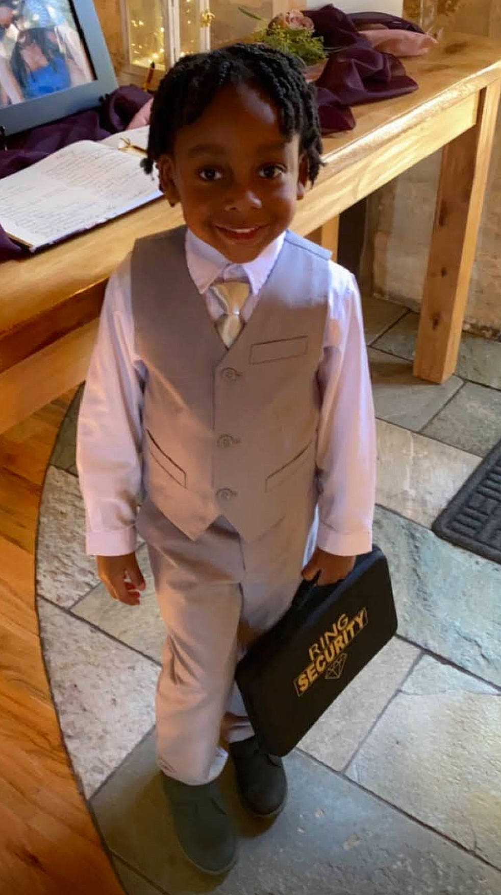 Hasani is registered to the contest to win money with this photo: blazer, chair, collar, desk, dress_shirt, flooring, formal_wear, hardwood, joy, person, room, school_uniform, sleeve, smile, suit, table, tie, toddler, uniform, varnish