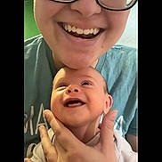 Astrid is registered to the contest to win money with this photo: adult, baby, smile, glasses, hand, face, person, joy, holding, happy, indoor, casual, portrait, closeup, infant, family, tshirt, skin, expression, together