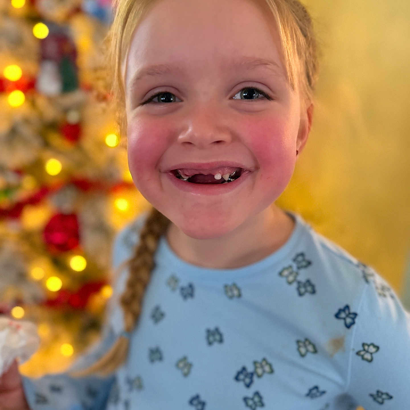 Alaya joined the competition — help win amazing prizes! background_blur, blue_shirt, braid, butterfly_pattern, child, christmas_tree, close_up, face, festive, happy, holiday_lights, indoor, long_hair, missing_tooth, person, portrait, seasonal, smiling, warm_lighting, young_girl