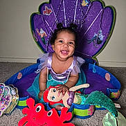 Kailani is registered to the contest to win money with this photo: toddler, child, smiling, plush_toy, mermaid_costume, purple_backdrop, seashell, carpet, indoor, cute, happy, doll, red_crab, costume, playtime, decor, portrait, baby, fun, bright