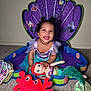 toddler, child, smiling, plush_toy, mermaid_costume, purple_backdrop, seashell, carpet, indoor, cute, happy, doll, red_crab, costume, playtime, decor, portrait, baby, fun, bright