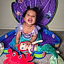 baby, child, smiling, mermaid, costume, plush_toy, doll, red_crab, purple_shell, carpet, indoor, happy, cute, playful, fantasy, underwater_theme, blue_tulle, curly_hair, portrait, decorative