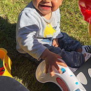 Lino participe au concours pour gagner de l'argent avec cette photo : toddler, child, smiling, outdoor, grass, toy, cap, sweater, sunlight, happy, play, person, baby, nature, daylight, casual_clothing, young_child, reaching, sitting, cute