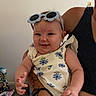 baby, child, sunglasses, floral_dress, tattoo, smiling, indoor, person, arm, carpet, adult, holding, cute, happy, flower_pattern, casual, home, furniture, accessory, infant