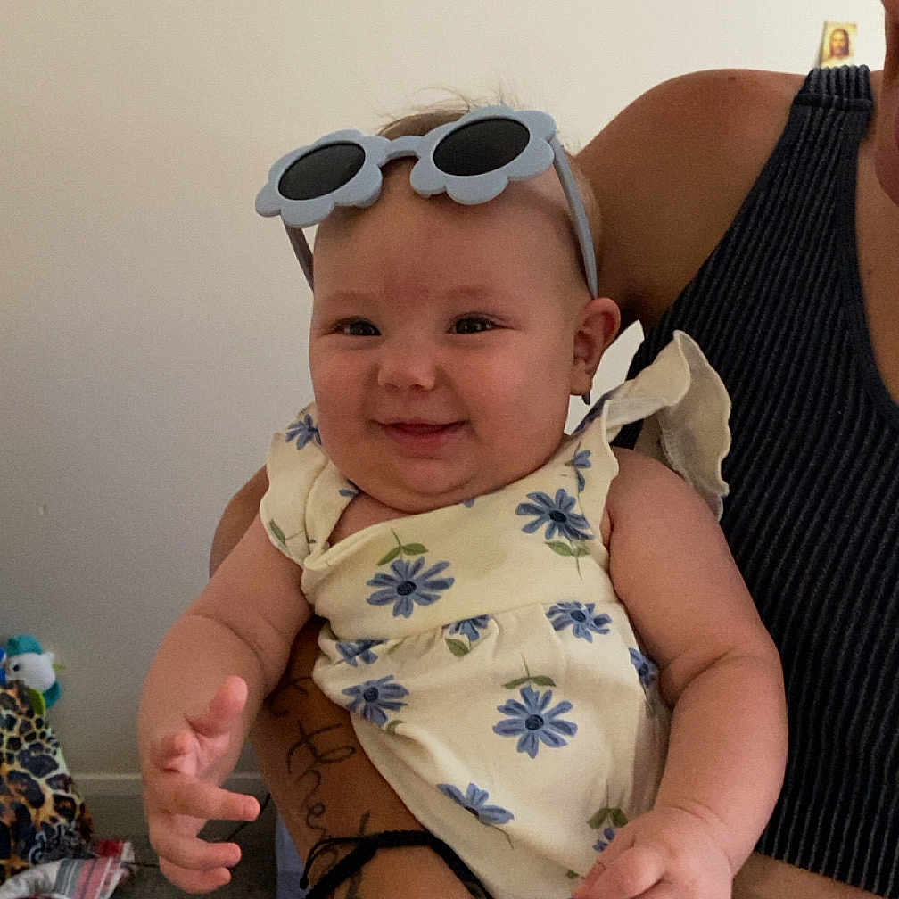 Wrenlee joined the competition — help win amazing prizes! baby, child, sunglasses, floral_dress, tattoo, smiling, indoor, person, arm, carpet, adult, holding, cute, happy, flower_pattern, casual, home, furniture, accessory, infant