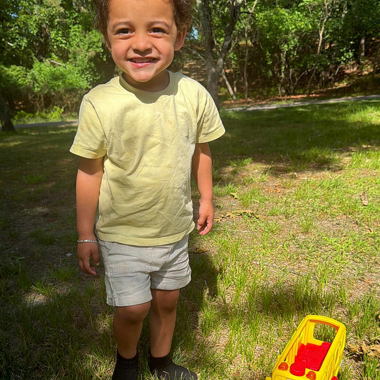 Randolph joined the competition — help win amazing prizes! child, smiling, outdoor, grass, trees, toy, yellow_toy, shorts, tshirt, sunlight, nature, happy, play, boy, forest, daylight, feet, shadow, casual_clothing, park